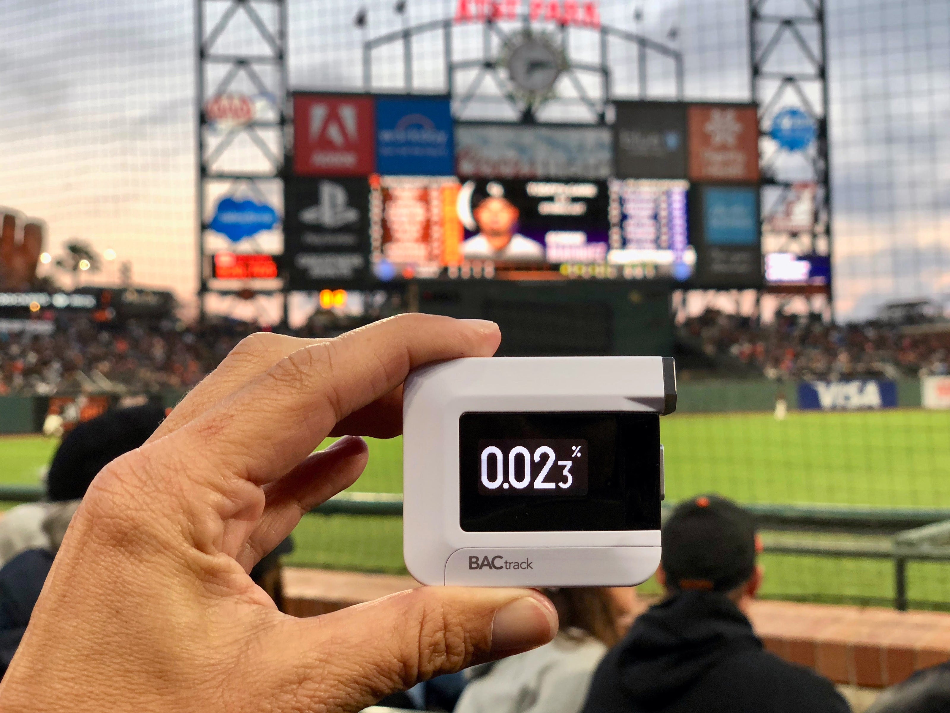 Hand holding a BACtrack breathalyzer showing a 0.023% BAC reading at a baseball stadium